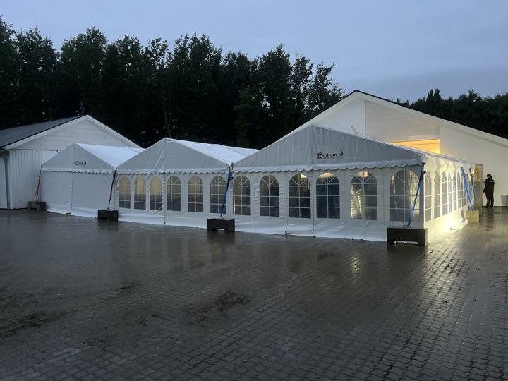 Sammenbyggede festtelte med lys indeni på en gårdsplads i skumringen